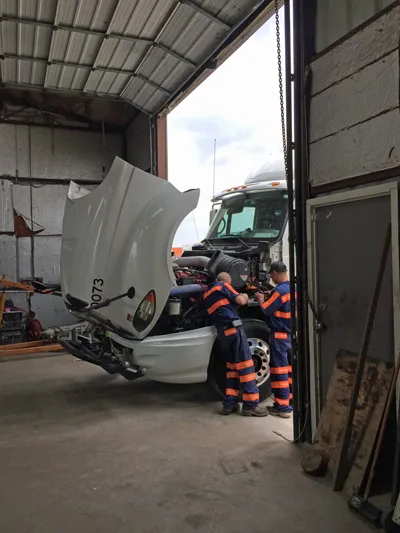 Two SDR technicians servicing a diesel truck engine with the hood raised